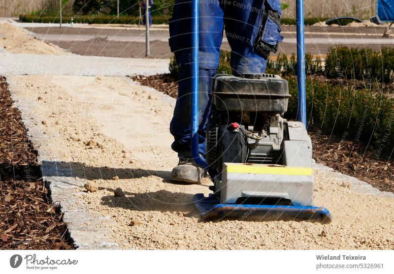 Legs and feet of a man who operates a sand compactor. The man is vibrating the sand of a new path. blue soil outdoor people outdoors male plate equipment work