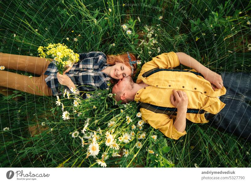 happy young couple man and redhead woman lying on bright green grass on summer day, top view. Love story. together girl female happiness love beautiful people