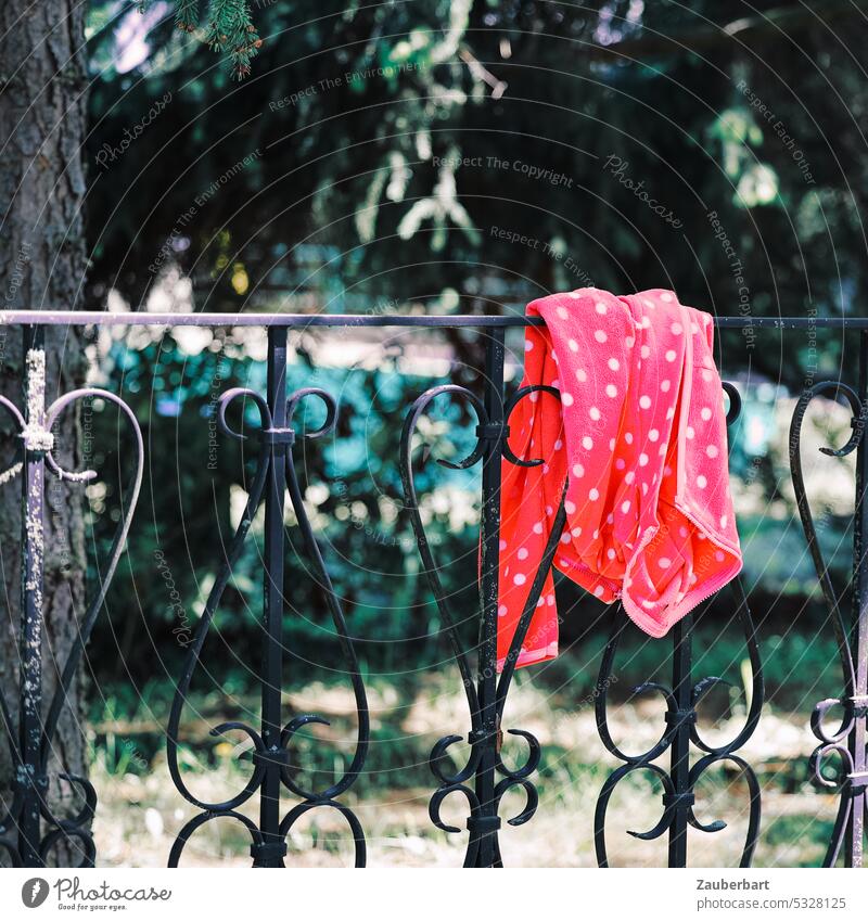 A red jacket with white dots lies over a wrought iron fence Jacket Red points White Fence forged Hang Doomed Forget found lost property office Child Infancy