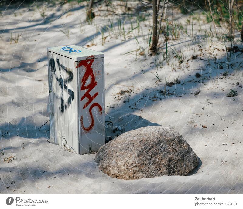 Switch box with graffiti stands next to boulder on beach switch box Graffiti foundling Beach Sand Shadow Sun Disagreement technique Nature Disfigurement