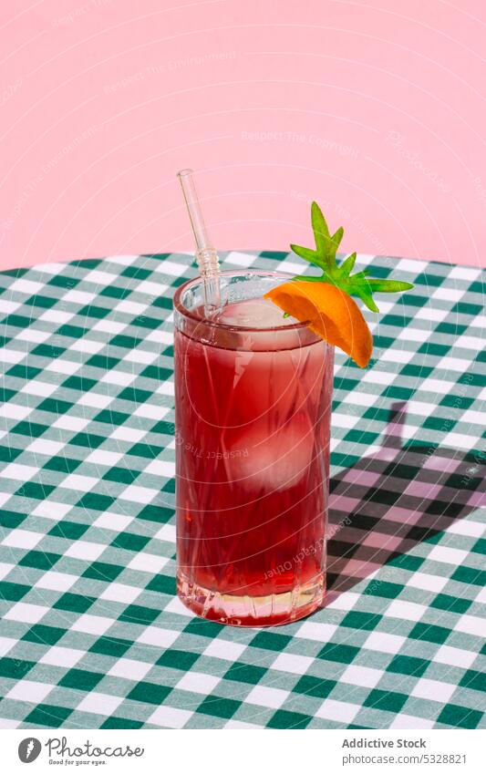 Glass of red cocktail with orange slice glass drink beverage refreshment table serve cold straw delicious checkered citrus fruit alcohol transparent tasty