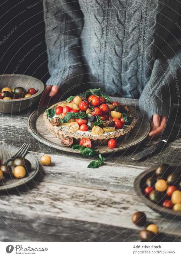 Crop person with tart served with cherry tomatoes and herbs pie plate food vegetable healthy delicious fresh tasty meal baked dish ripe yummy appetizing cuisine