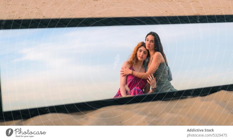 Calm women resting on sandy beach together mirror reflection hug friend summer pensive thoughtful friendship female young calm nature embrace peaceful coast