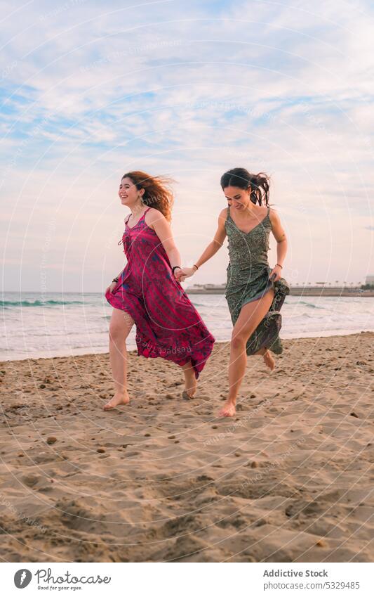 Happy women running on sandy beach friend happy holding hands cheerful sea friendship seaside barefoot summer together carefree vacation dress smile nature sun