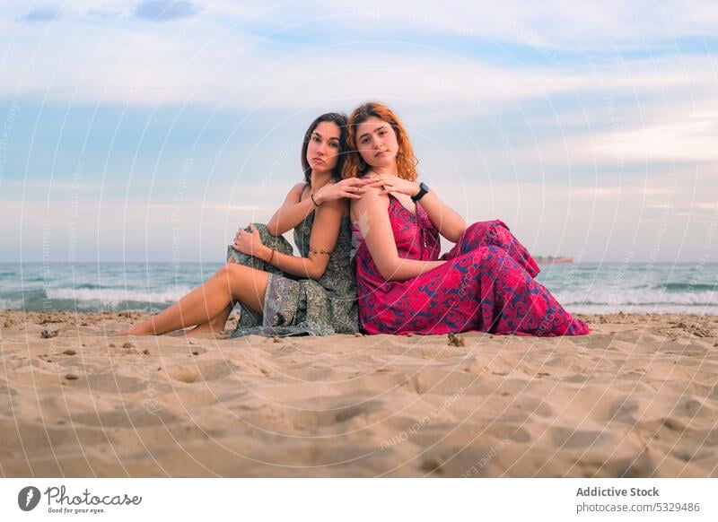 Women sitting together on seashore women friend friendship beach summer sand vacation back to back sunset coast pensive thoughtful female water ocean nature