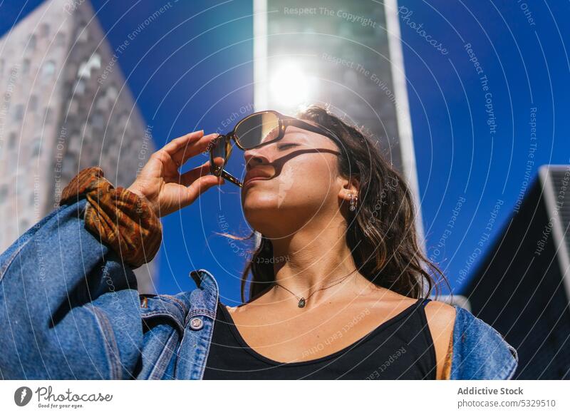 Stylish woman in sunglasses on street on sunny day city style skyscraper district urban megapolis jacket take off eyes closed modern female building casual
