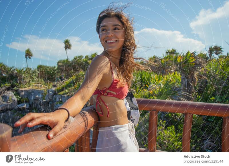 Smiling woman standing near railing smile rest lean relax happy vacation resort holiday cheerful tropical summer joy positive young swimwear plant female
