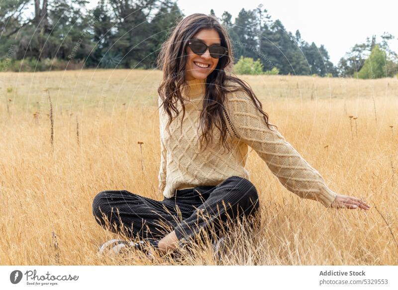 Smiling woman in sunglasses resting on dry grass field meadow nature countryside wave hand sunlight relax cheerful happy female plant enjoy smile style bright