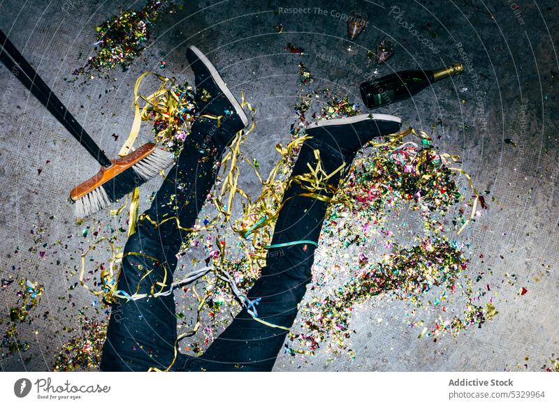 Crop drunk man with confetti on floor during party celebrate booze festive holiday champagne tired messy broom lying colored paper casual wear glow alone