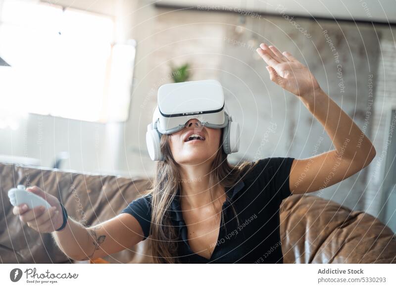 Woman in VR headset interacting with digital world using controllers woman videogame vr play virtual reality sofa home experience gadget device living room
