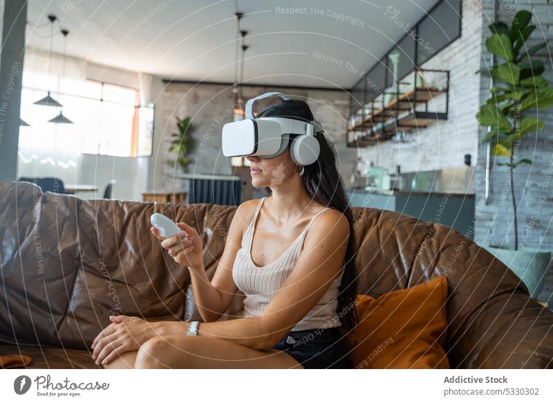 Woman in VR headset interacting with digital world using controllers woman videogame vr play virtual reality sofa home experience gadget device living room