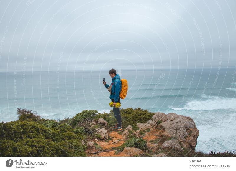 Adventurer wandering the Fisherman Trail in the Algarve region of Portugal takes pictures of the ocean, which has come to life during the rainy weather. The power of water