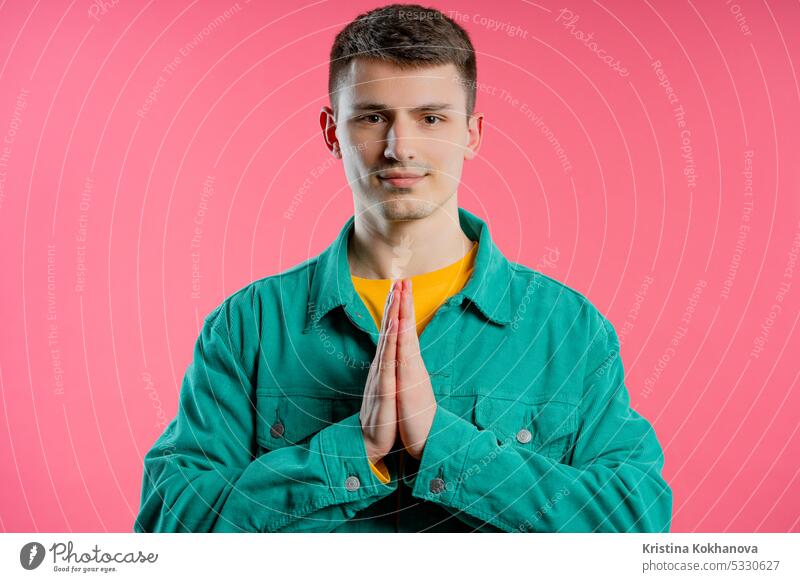 Young man praying, begs on pink background. Hopeful prayer asks to help with hope hands belief faith god religion young adult person please people wish