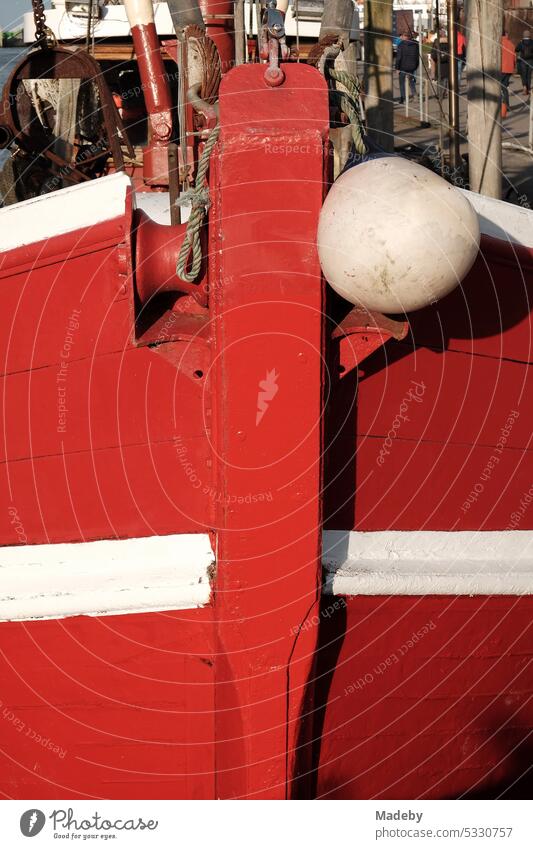 Bow of an old red fishing boat with white stripe in the sunshine in the harbor of Neuharlingersiel on the coast of the North Sea near Esens in East Frisia in Lower Saxony