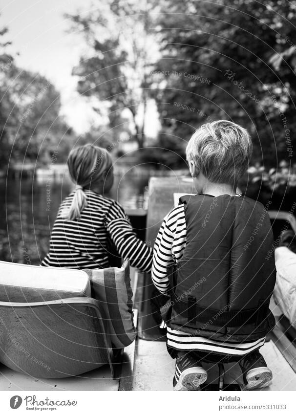 Back view of two children on a pedal boat on a lake Infancy Pedalo Water Trip Sit Crouch Stripe bank steer Tread Life jacket trees Lake Vacation & Travel