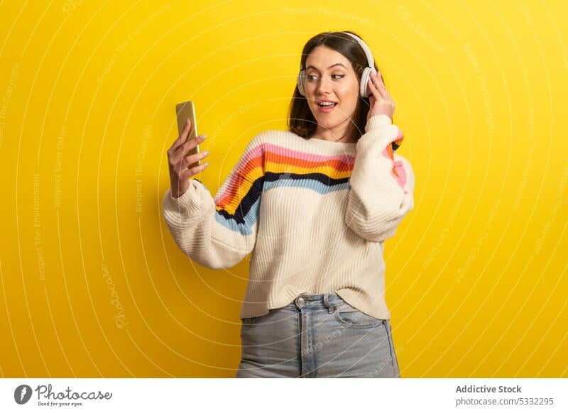 Smiling woman with smartphone listening to music on yellow background headphones smile happy device cheerful positive modern wireless female young bright casual