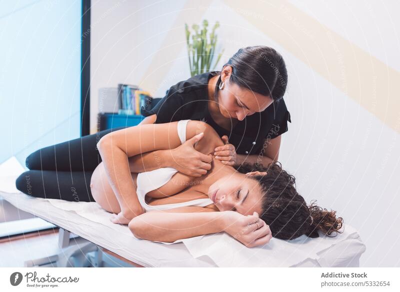 Masseuse doing massage to pregnant client on table woman osteopath masseur patient procedure press treat therapy clinic shoulder finger rehabilitation