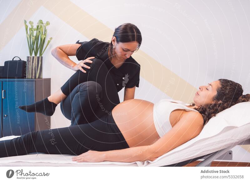 Masseuse doing massage to pregnant client on bench woman masseur patient osteopath therapy rehabilitation physiotherapy clinic leg raised treat recovery