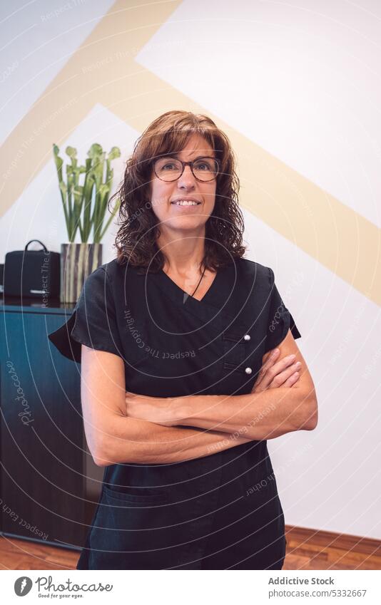 Confident woman with crossed arms looking at camera and smiling doctor physiotherapist osteopath smile uniform eyeglasses clinic arms crossed professional