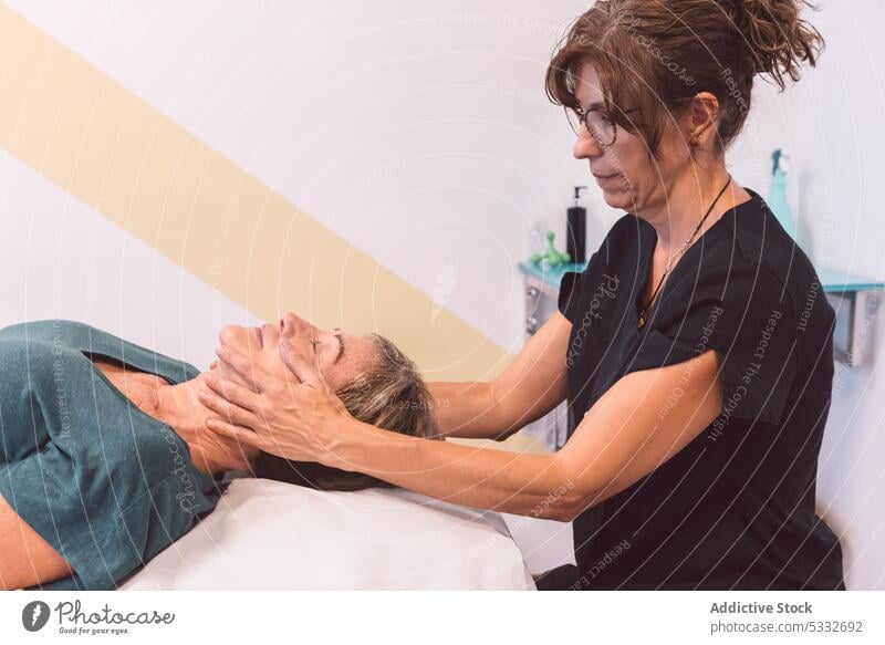 Masseuse doing massage to face of client woman physiotherapist osteopath patient head procedure therapy lying rehabilitation treat female specialist relax ache