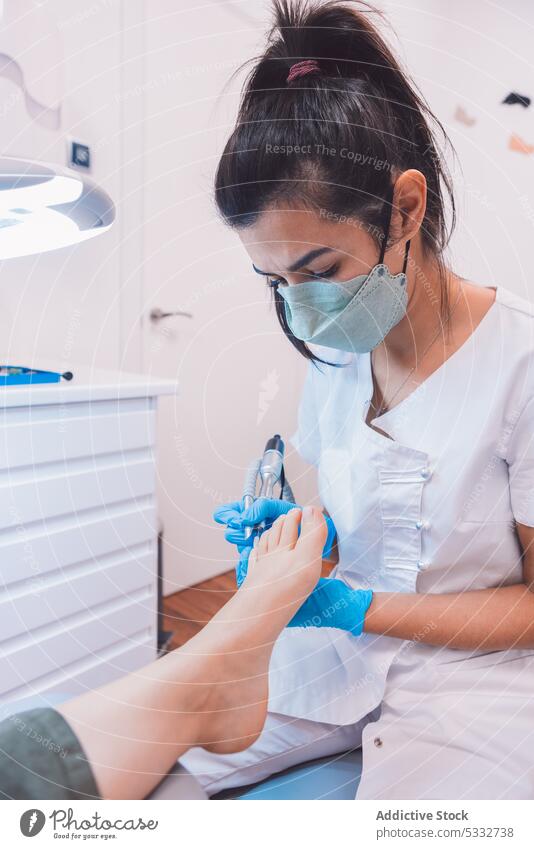 Serious podiatrist doing pedicure with professional equipment woman clinic heal tool salon mask procedure modern protect treat doctor foot treatment patient