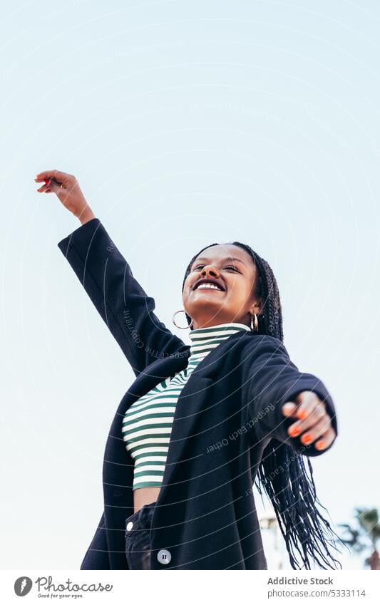 Cheerful black woman with raised arms cheerful smile braid happy positive joy street laugh arm raised style young female glad optimist hand raised hairstyle