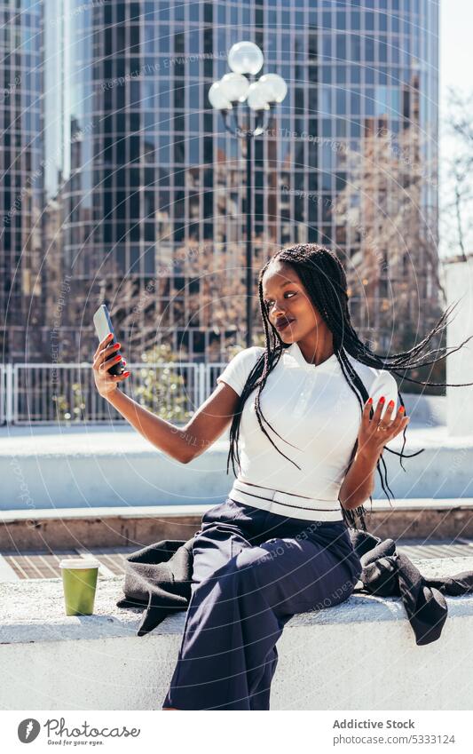 Black woman taking selfie on smartphone using self portrait street device mobile cellphone take photo city bench casual african american female ethnic young sit