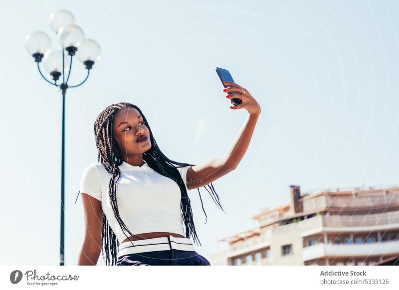Black woman taking selfie on smartphone using self portrait street device mobile cellphone take photo city bench casual african american female ethnic young sit