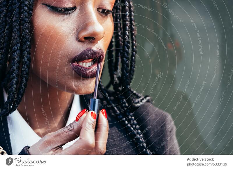 Black woman applying lipstick on street makeup using braid device mobile visage african american female ethnic black afro feminine appearance hairstyle trendy