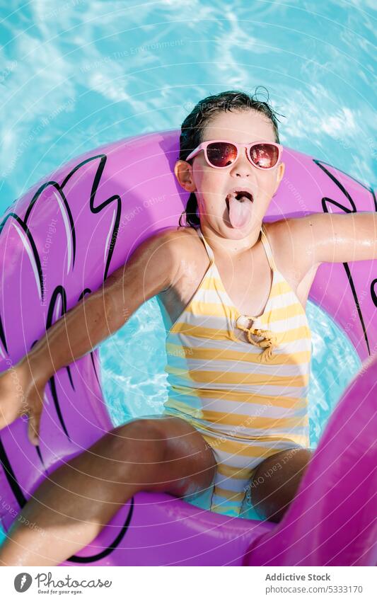 Little child resting in swimming pool girl water stick out tongue relax kid float inflatable summer holiday ring vacation resort tube swimsuit childhood