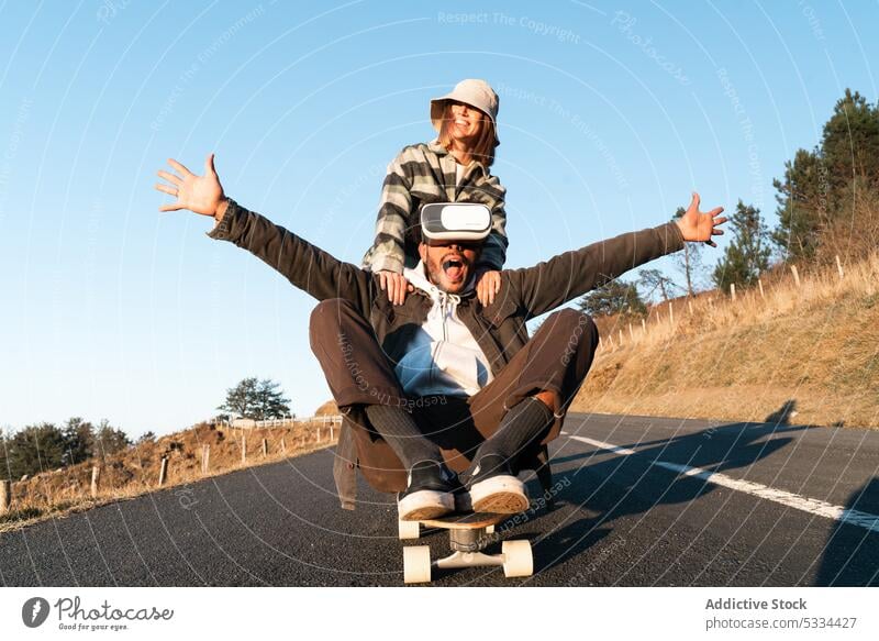 Happy man and woman with skateboard having fun on road couple leisure virtual reality together spend time skater activity goggles nature device mountain freedom