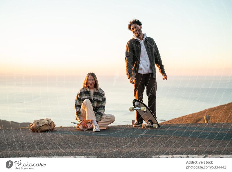 Happy multiethnic couple with skateboards having fun together on road smile sunset happy relationship love skater cheerful beach sea spend time multiracial
