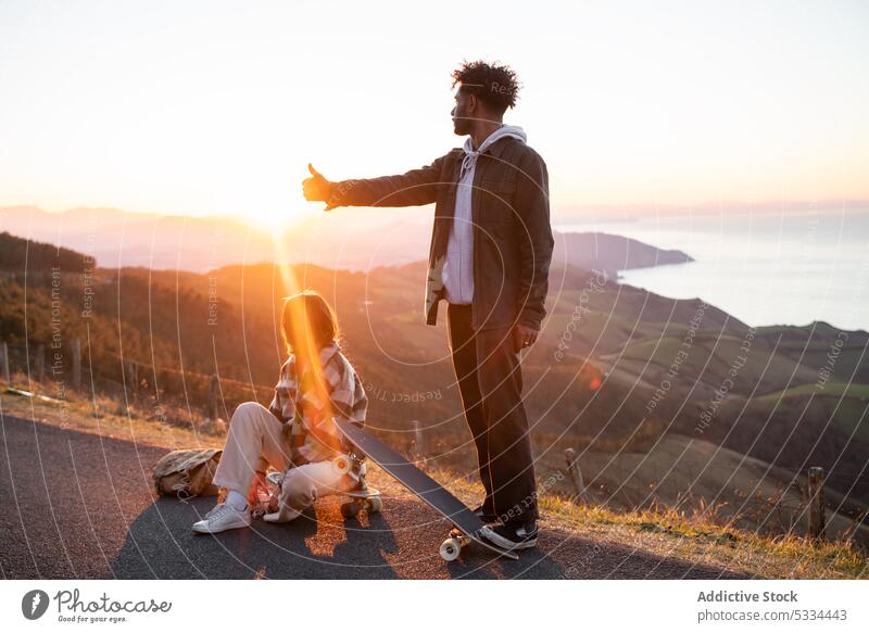 Side view of diverse young couple with skateboards on road in mountains during sundown thumb up sunset gesture together relationship evening skater cool nature