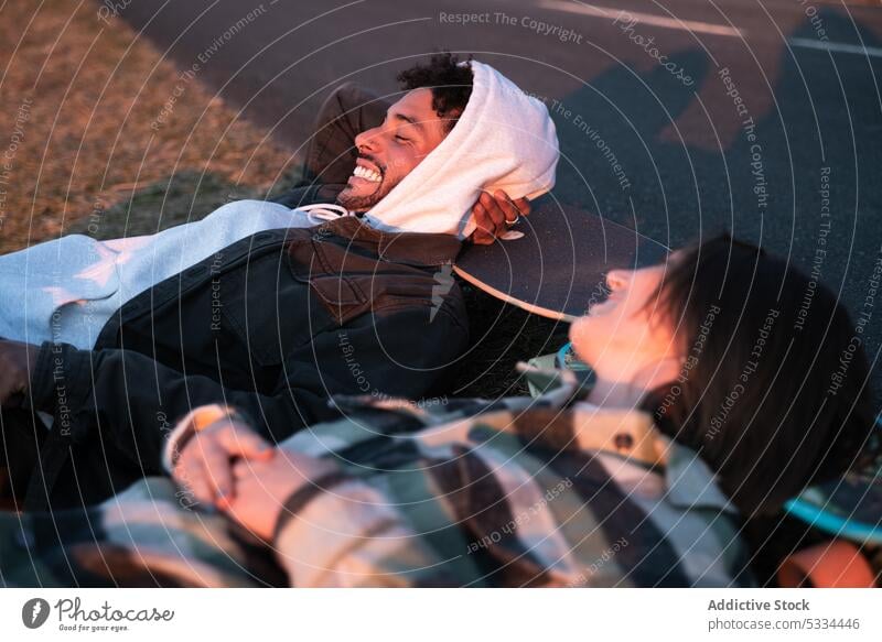 Positive young diverse man and woman lying on grass with skateboards couple laugh nature relax love happy relationship together cheerful carefree rest