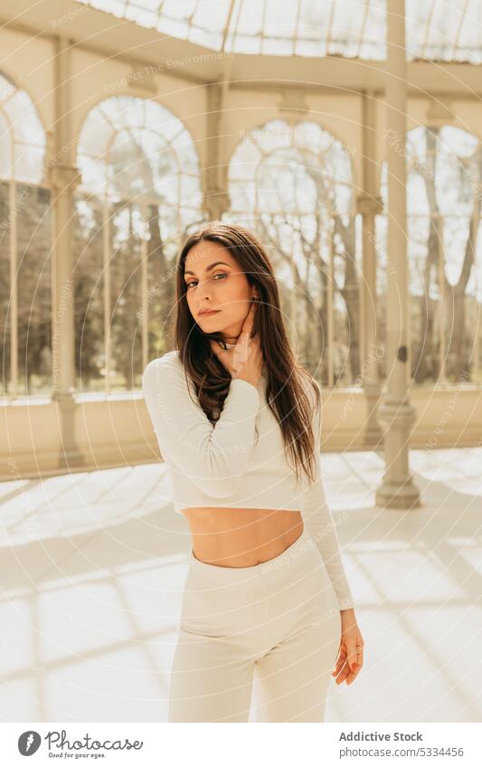 Calm sportive woman standing in light hallway of palace appearance charming brunette long hair calm tranquil serene confident building glass palace activewear