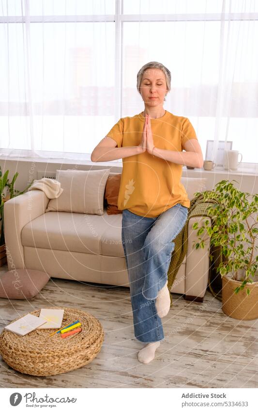 Adult woman meditating at home in daylight meditate yoga balance practice exercise wellness training sofa plant flexible chemotherapy survivor cancer recovery