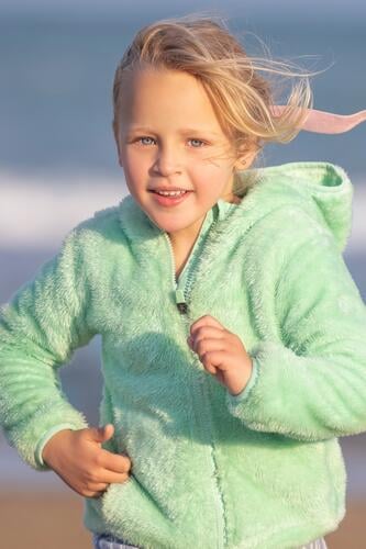 A 5-year-old girl in a green jacket is running child childhood blonde 5 years old beach sea sand ocean coast vertical young eyes blue holiday lifestyle sky