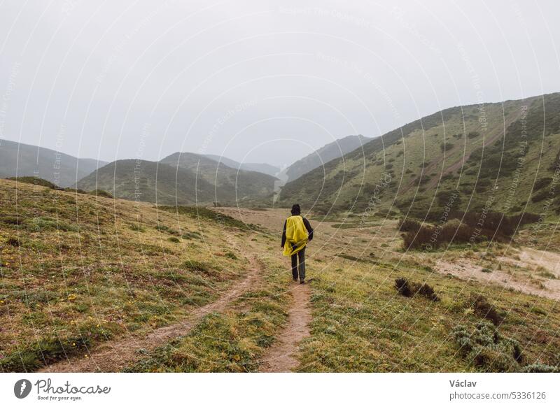Wandering in heavy rain and wearing a raincoat along the Fisherman Trail in the southern part of Portugal during rainy weather heading to Cape St. Vicente. Rough landscape