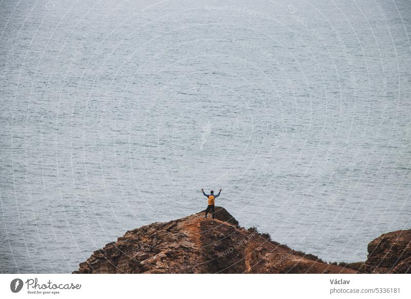 Adventurous man standing on the edge of a cliff enjoys the view of the Atlantic coast in the Odemira region of southwestern Portugal. Wandering the Rota Vicentina