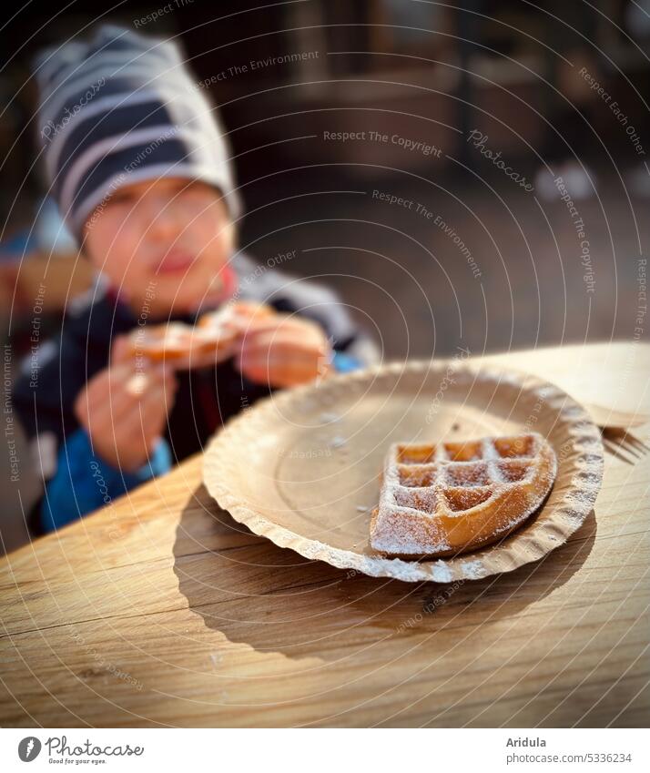 Plate with waffle and powdered sugar, in the background a child eats a piece of waffle Waffle Confectioner`s sugar cute Delicious Nutrition Food Candy