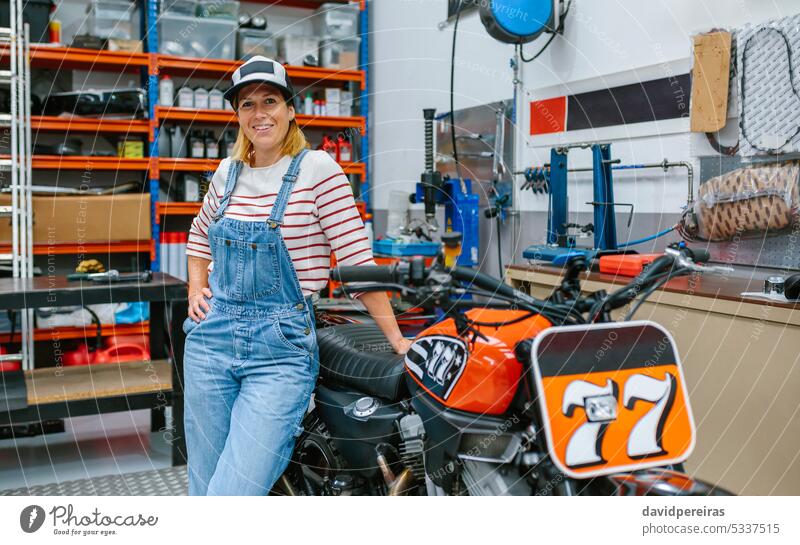 Mechanic woman standing on motorcycle factory female mechanic motorbike workshop smile smiling friendly happiness happy looking camera garage profession worker