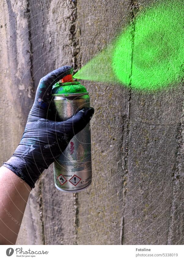 A hand, protected by a black disposable glove, presses down the button of a spray can and sprays a gray wall bright green. Something colorless just give a new hue!.