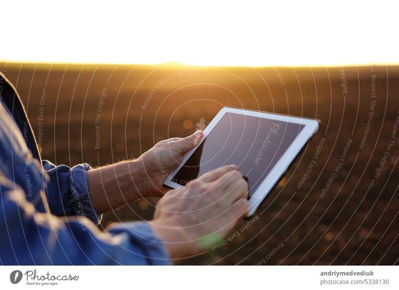 Cropped shot of male farmer's hands use digital tablet on plowed field for control of soil quality, land readiness for sowing crops and planting vegetables. Smart farming technology and agriculture