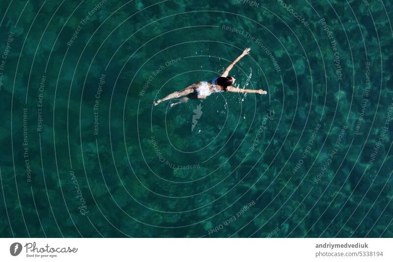 Above view of woman swimming at sea. Aerial top view of young girl in white swimsuit floating on water surface in crystal clear turquoise sea. Vacation at Paradise. Ocean relax, travel and vacation