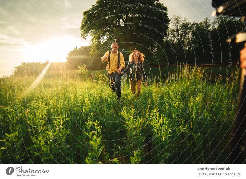 Loving hipster couple walking in the field, kissing and holding hands, hugging, lying in the grass in the summer at sunset. valentines day man love relationship