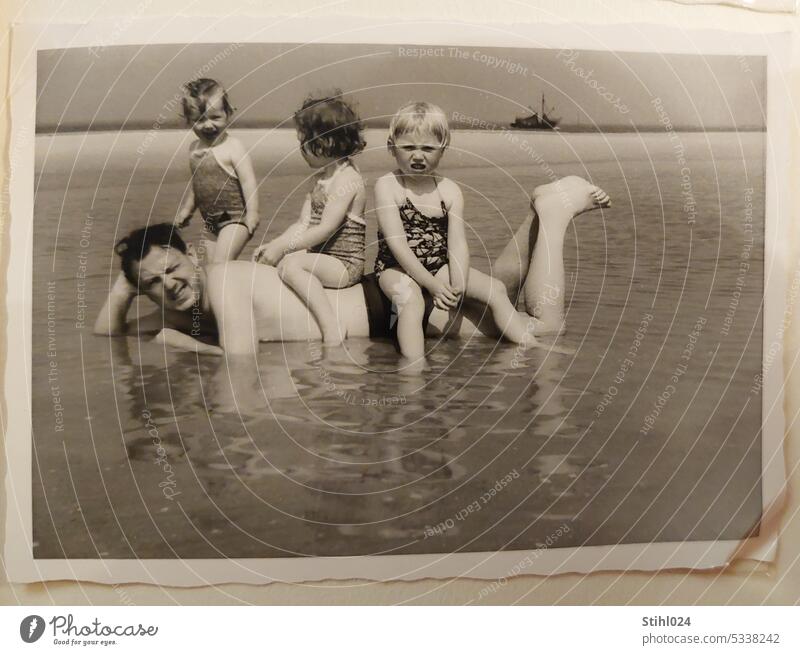 Children sitting on lying father on sandy beach - father with children vacation on beach Father Sit bathe relaxed Sandy beach Water North Sea fifties