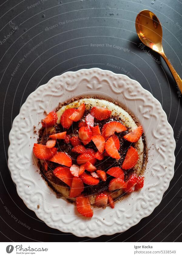 Full plate of porridge with fresh cut strawberries, sprinkled with cocoa powder, on a black table with golden spoon. strawberry food fruit vegetarian health