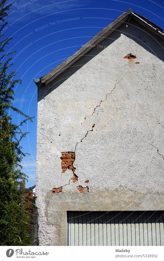Old facade of a residential house with crumbling plaster, pointed gable and garage in front of blue sky in the sunshine in Wettenberg Krofdorf-Gleiberg near Giessen in Hesse, Germany