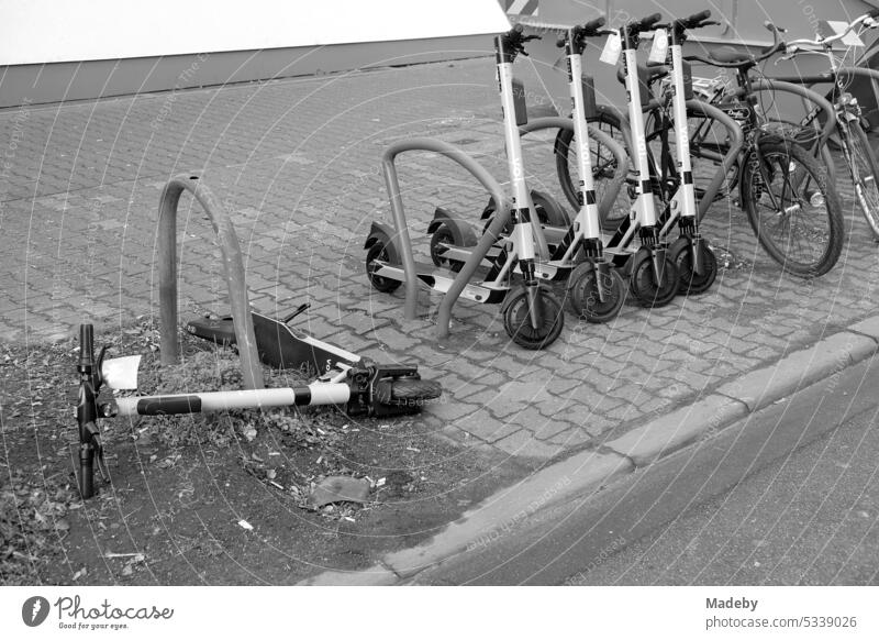 Overturned tourist e-scooter on the composite sidewalk of a sidewalk in Friedberger Landstraße in the north end of Frankfurt am Main in Hesse in neo-realistic black and white
