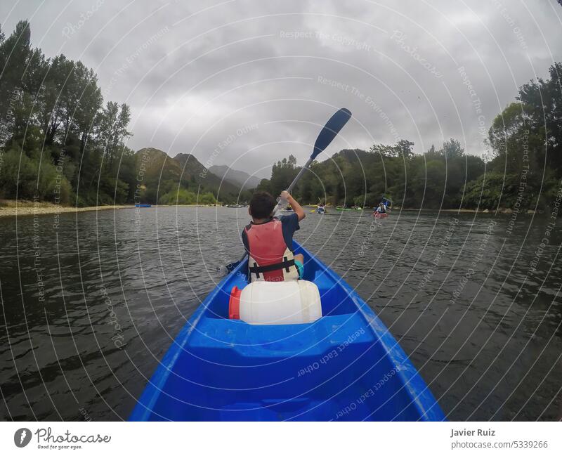 a young canoeist seen from behind paddling a kayak on a wide river with other canoeists out of focus in the background, descent of the river Sella kayaking